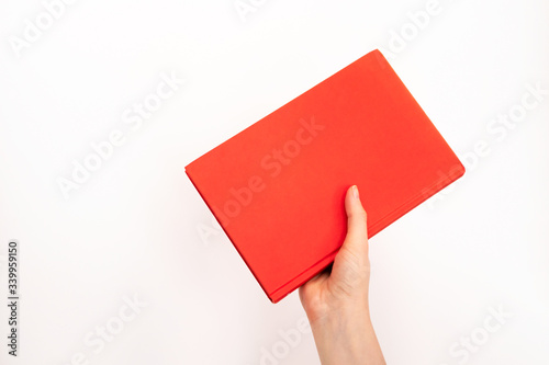 Hand holding book in red cover with selective focus on white background and copy space. Concept education, learning and studying