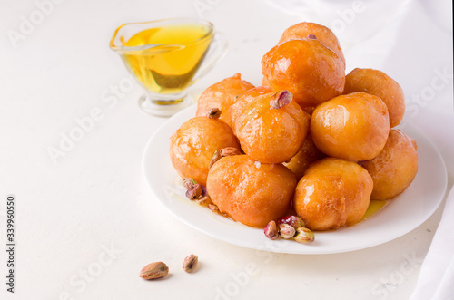 Arabic sweet round dessert Lokma with nuts on a white plate. Copy space