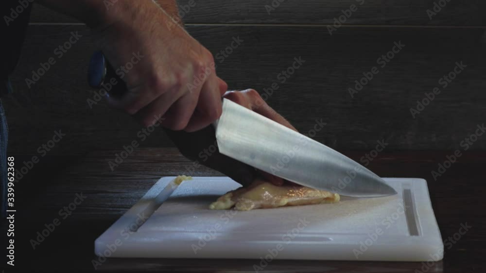 Dramatic chef cuts raw chicken fat in food prep side angle Dramatic chef cuts raw chicken fat in food prep side angle