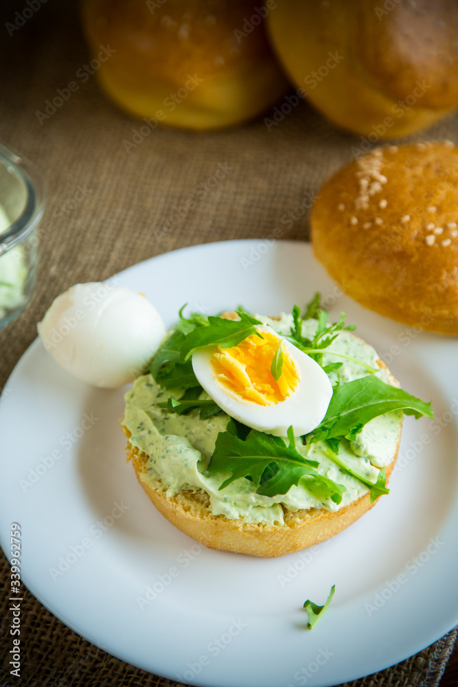 Homemade bun with cheese spread, fresh arugula and boiled egg in a plate