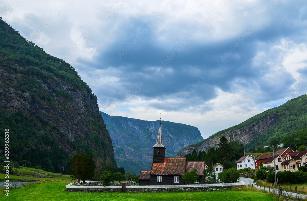 View of the Old wooden Flam Church or Flam Kyrkje and beautiful mountains on background on a cloudy summer day. Sognefjord, Norway
