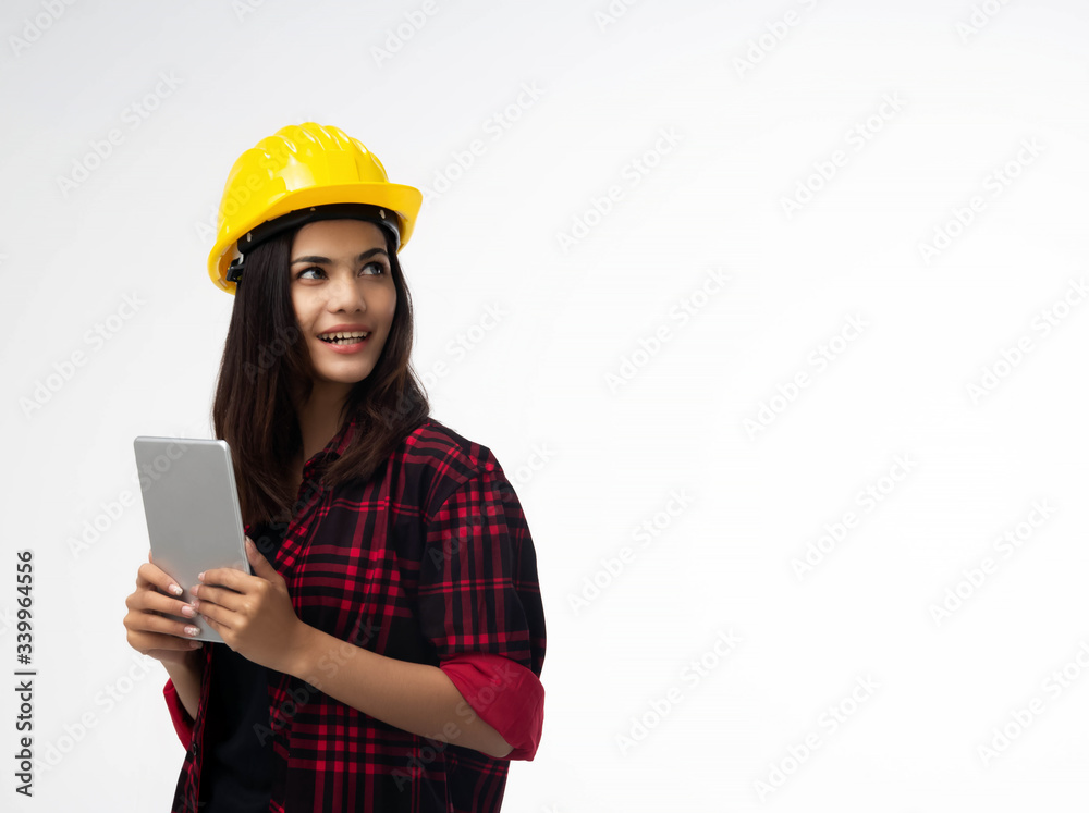 Young woman engineer standing at the left side of background,wearing yellow safety helmet ,holding tabletn hand,littler smile,portrait of model posing Young woman engineer standing at the left side of background,wearing yellow safety helmet ,holding tabletn hand,littler smile,portrait of model posing