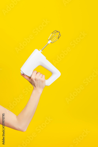 White kitchen mixer in female hand isolated on bright yellow background