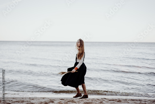 Fototapeta Naklejka Na Ścianę i Meble -  A girl in a black dress and white shirt walks along a deserted seashore in calm weather and completely calm