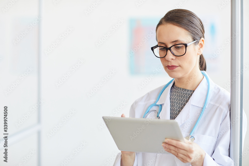 Young female doctor in eyeglasses wearing white coat and using digital tablet at hospital Young female doctor in eyeglasses wearing white coat and using digital tablet at hospital