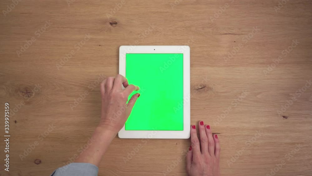 Top view of a woman's hands using a chroma green screen tablet on a wooden desk Top view of a woman's hands using a chroma green screen tablet on a wooden desk