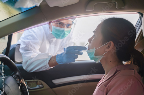 Medical worker in protective suit screening woman Driver to Sampling secretion to check for Covid-19. Drive thru test coronavirus fast track. Concept prevention coronavirus outbreak.