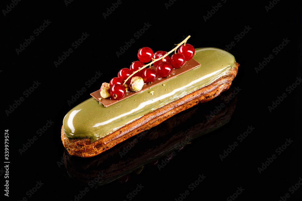 Eclair with cream filling and elegant decorative cranberry topping coated with pistachio glaze. Confectionary photography concept in black background. Eclair with cream filling and elegant decorative cranberry topping coated with pistachio glaze. Confectionary photography concept in black background.