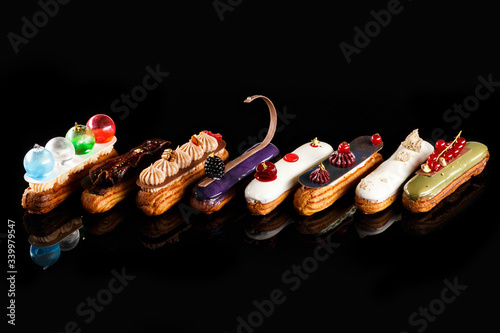 Assorted eclairs with cream filling and elegant decorative toppings for confectionary photography concept in black background. Luxury desserts photo