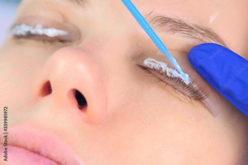 Beautician applying solution for lamination on woman lashes on curlers, lift eyelashes procedure in beauty salon, face closeup. Cosmetologist making lash lifting in cosmetology clinic, hands closeup.
