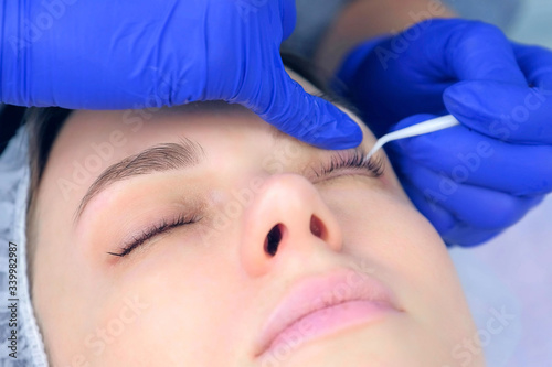 Cosmetologist separates woman's lashes using plastic brush and needle after laminating lifting procedure in beauty clinic. Beautician brushing eyelashes in cosmetology.