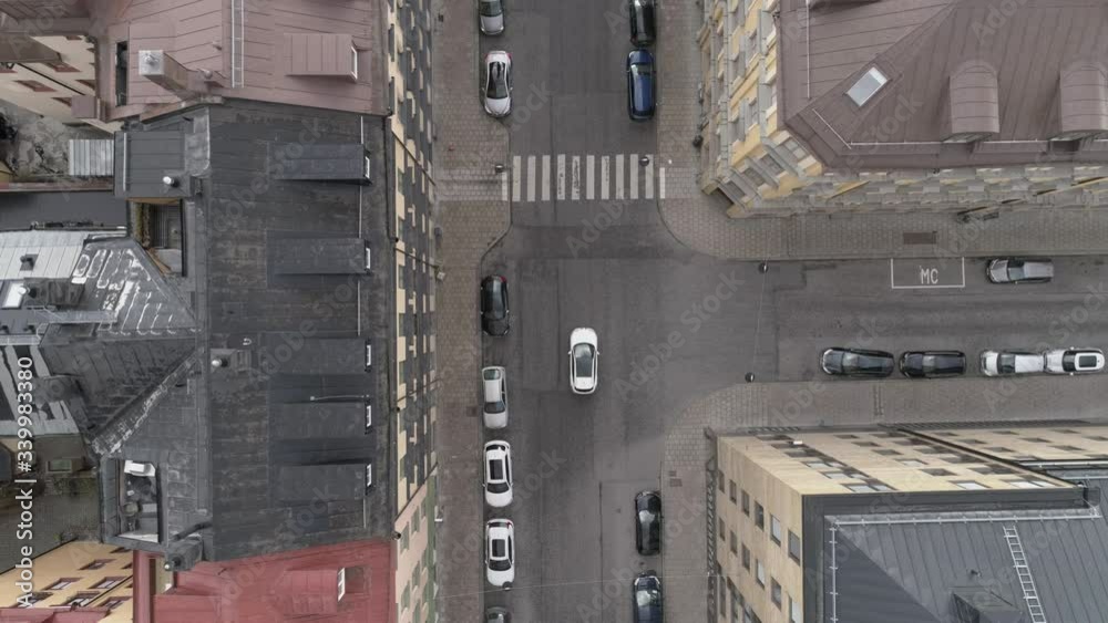 Aerial top down view of city street in Stockholm, Sweden. White car driving by. Drone shot flying over intersection, parked cars and buildings