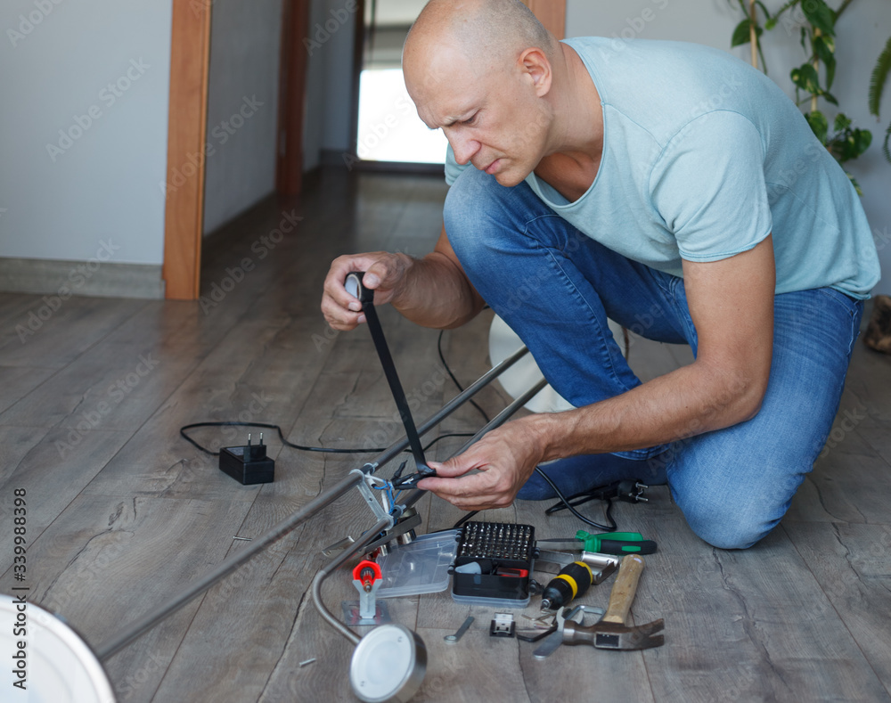 A man repairs a lamp while sitting on the floor of a house A man repairs a lamp while sitting on the floor of a house