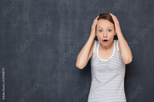 Portrait of surprised woman with widened eyes, holding hands on head