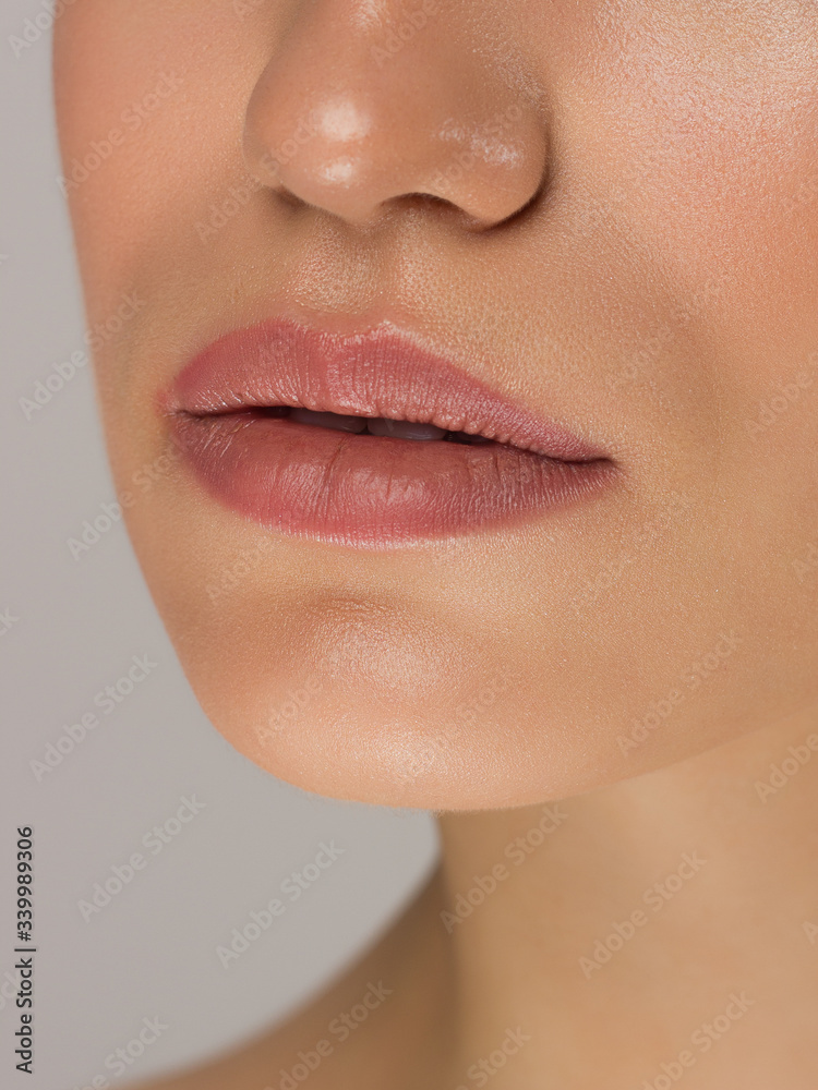 Obraz premium Cosmetics, makeup and trends. Bright lip gloss and lipstick on lips. Closeup of beautiful female mouth with natural lip makeup. Beautiful part of female face. Perfect clean skin in natural light