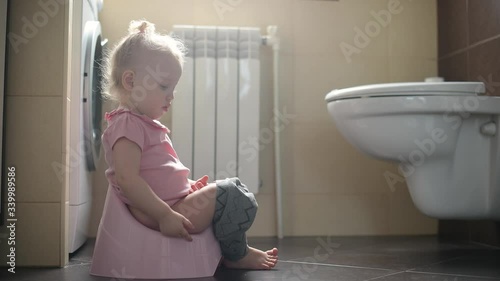 A little girl sits on a pot in the bathroom, side view