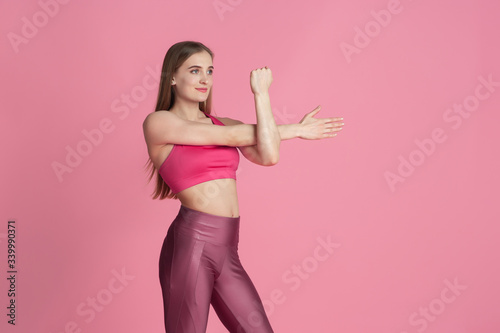 Graceful. Beautiful young female athlete practicing in studio, monochrome pink portrait. Sportive fit caucasian model posing. Body building, healthy lifestyle, beauty and action concept.