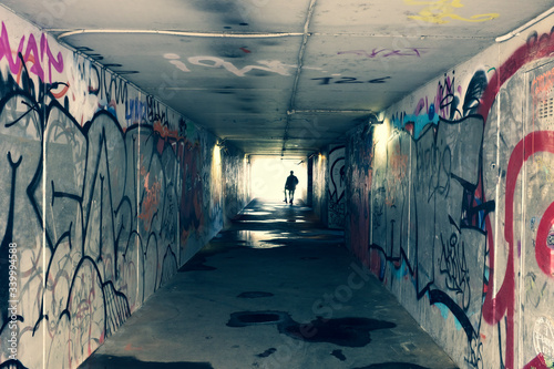 Mysterious light in the end of tunnel. Escape and exit to freedom and hope concept. Dark and long underground passage with light. Silhouette of a boy with skateboard in the end of tunnel. Ghetto area.