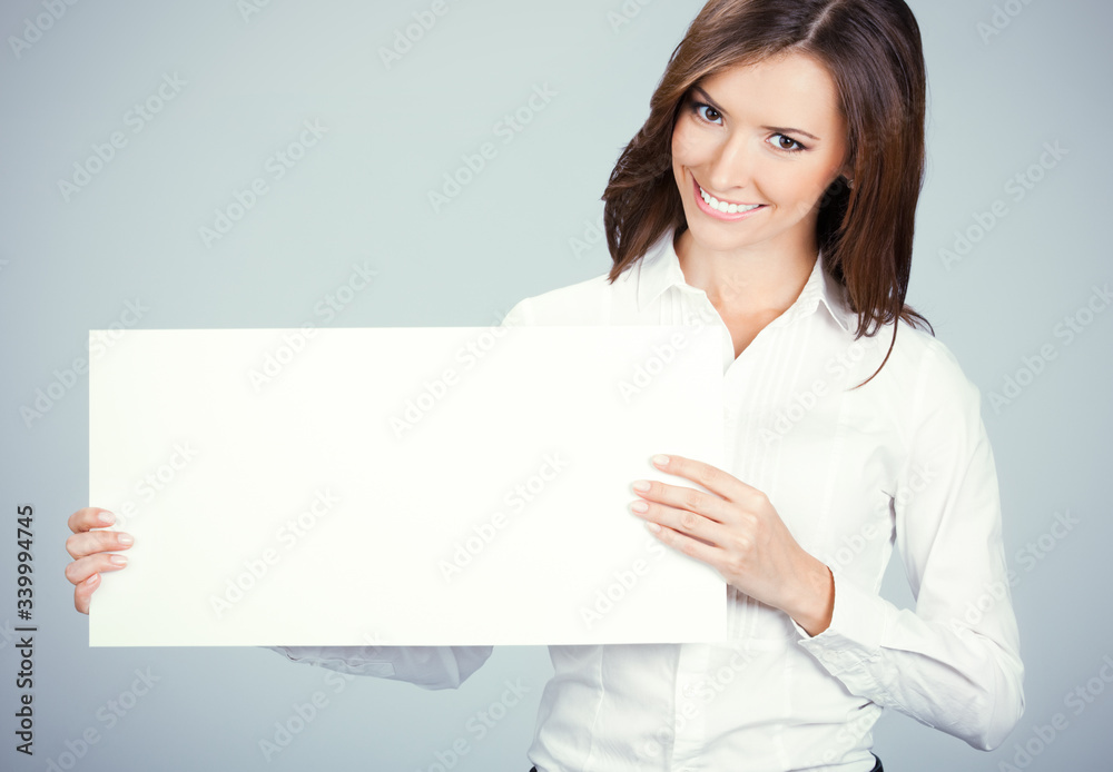 Smiling attractive woman showing blank sign board with empty copy space for some slogan, text or imaginary. Business ad concept. Multiracial Asian Chinese / Caucasian model over grey background. Smiling attractive woman showing blank sign board with empty copy space for some slogan, text or imaginary. Business ad concept. Multiracial Asian Chinese / Caucasian model over grey background.