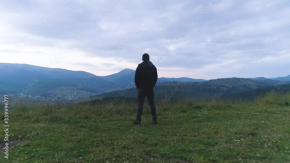 lonely young man standing on top of mountain, looking at sky with beautiful clouds and mountains at sunset. lonely young man standing on top of mountain, looking at sky with beautiful clouds and mountains at sunset.