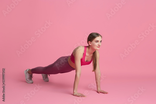 Plank balanced. Beautiful young female athlete practicing in studio, monochrome pink portrait. Sportive fit caucasian model training. Body building, healthy lifestyle, beauty and action concept.