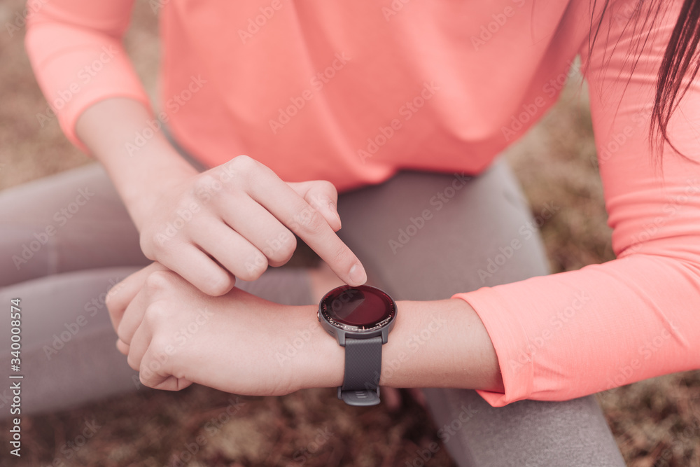 Person using smart watch. Young woman making gestures on a wearable smart watch computer device, smartwatch close up. Runner athlete checking heart rate monitor during workout on wearable smart watch.
