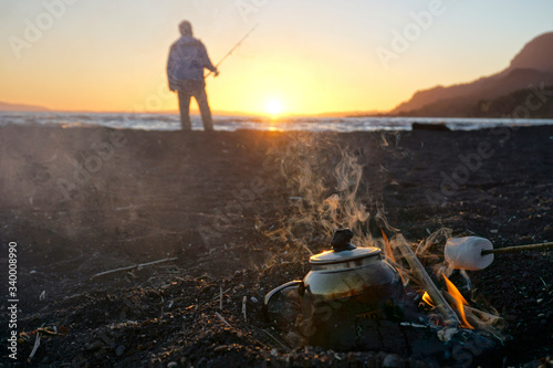 Teapot on fire and man fishing at sunset