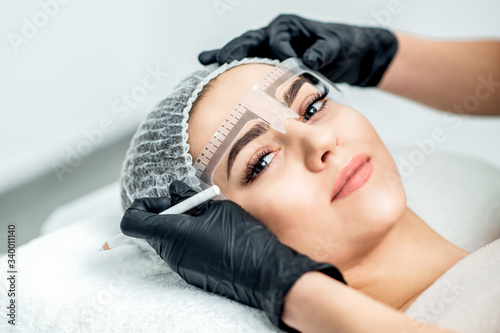 Markup with ruler on eyebrows of young woman during permanent make up. photo