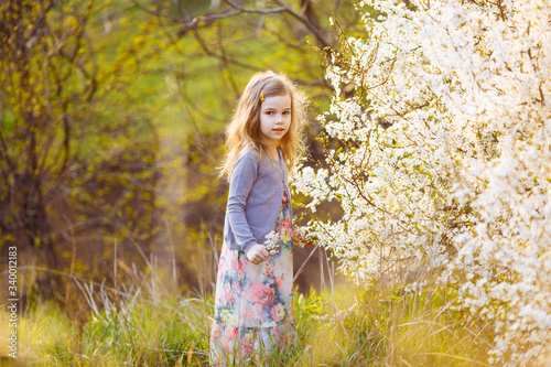 small girl next to flowers on a blooming shrub.