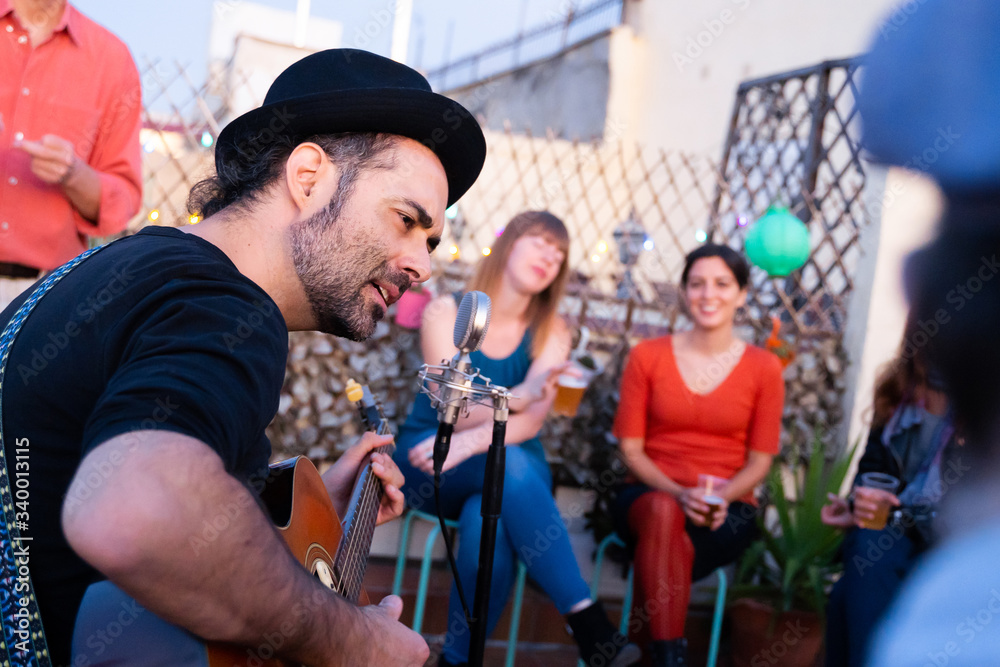 Lead singer of a rock band singing for audience on a rooftop. Portrait of a hipster male musician playing on an intimate concert. Man performing an acoustic guitar concert. Music live concerts concept