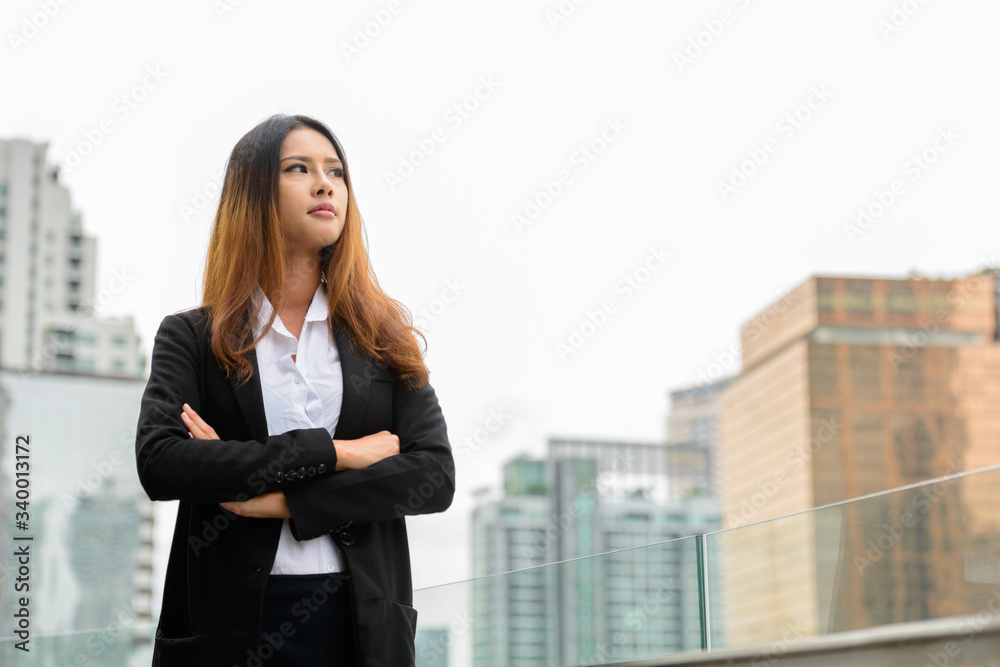 Young beautiful Asian businesswoman thinking against view of the city Young beautiful Asian businesswoman thinking against view of the city