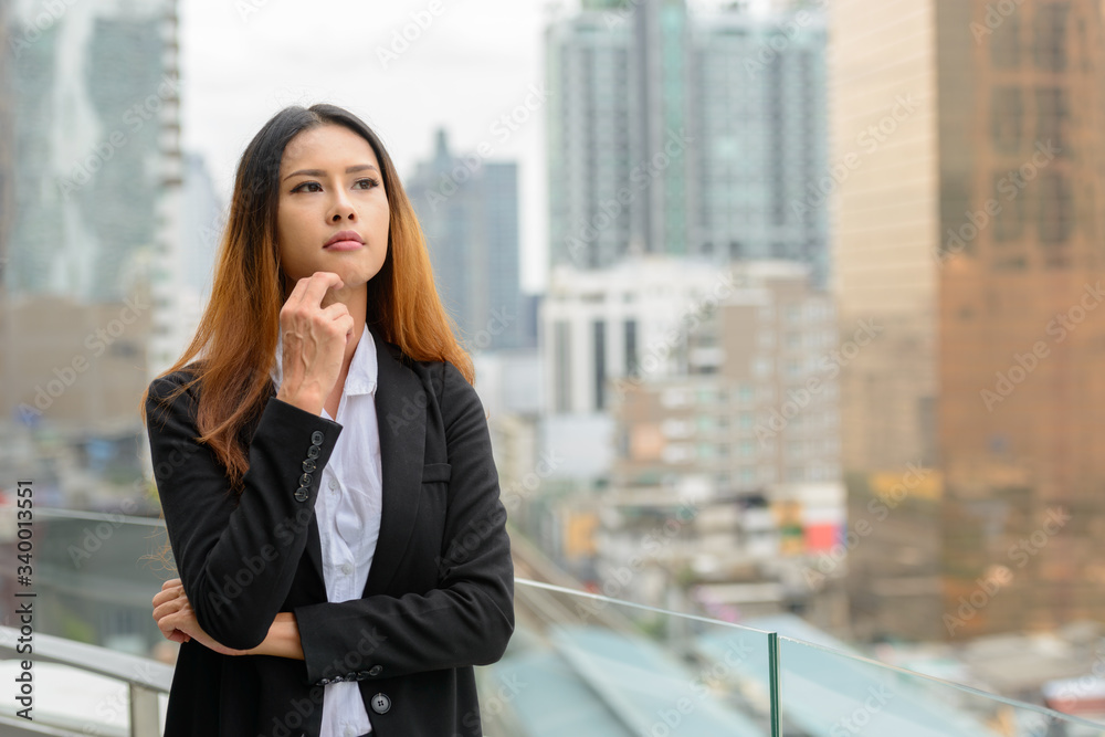 Young beautiful Asian businesswoman thinking against view of the city