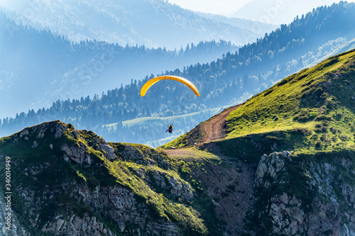 Yellow paraglider fly over mountain slope on sunny summer day,