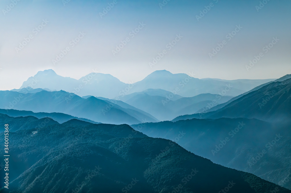 High mountains with green slopes in dense fog. Layers of mountains in the haze during sunset. Krasnaya Polyana, Sochi, Caucasus, Russia.
