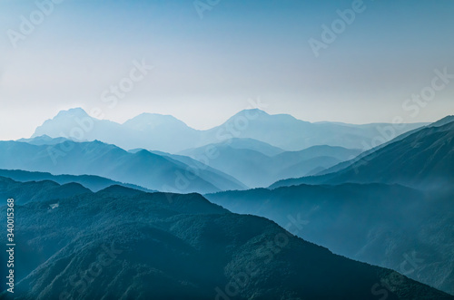 Fototapeta Naklejka Na Ścianę i Meble -  High mountains with green slopes in dense fog. Layers of mountains in the haze during sunset. Krasnaya Polyana, Sochi, Caucasus, Russia.
