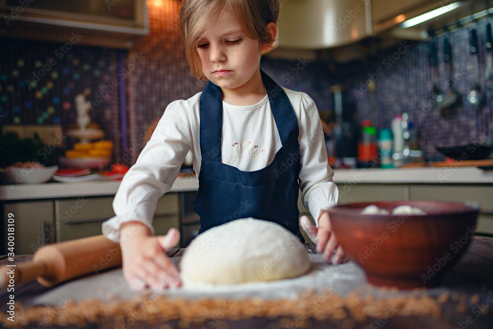 Little child girl with short hair haircut cooking dough in the kitchen. Horizontal indoors shot.