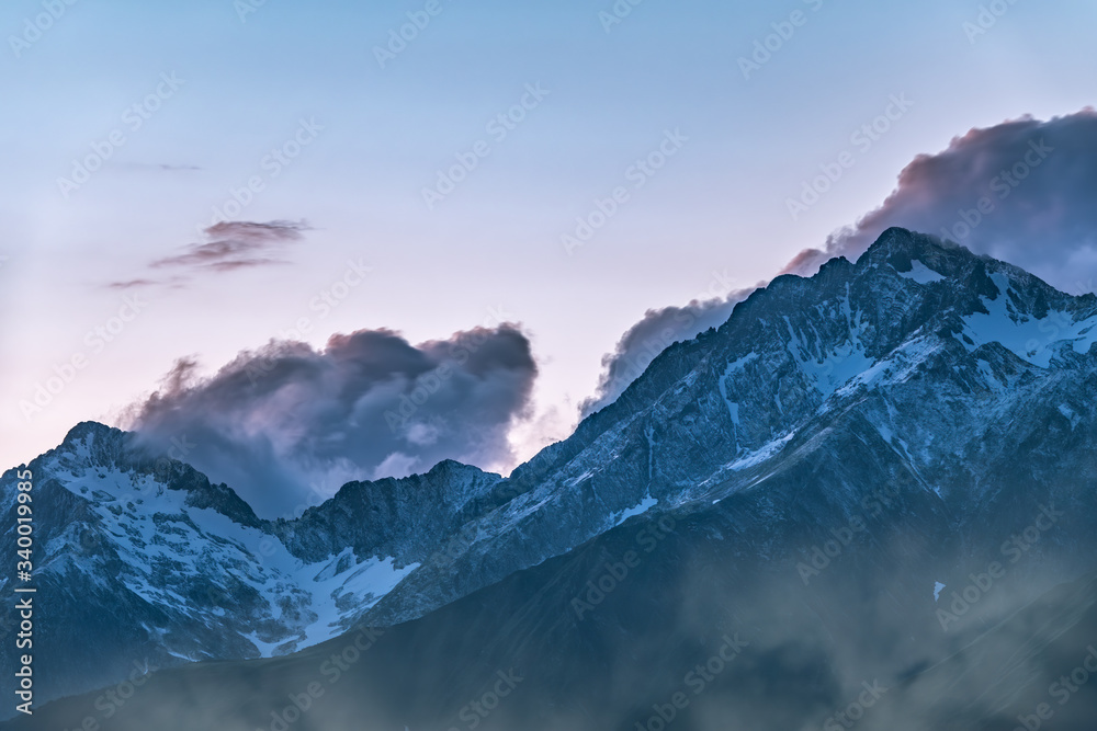 High mountains with snowy peaks at sunset in clouds and fog