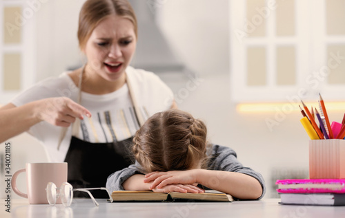Mother scolding her daughter while helping with homework in kitchen
