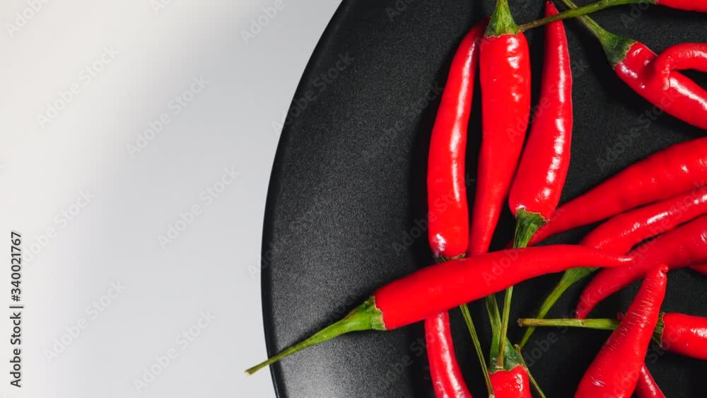 Top View Of Fresh Raw Red Chili Peppers Rotating On A Black Plate On A White Background On The Right Side.