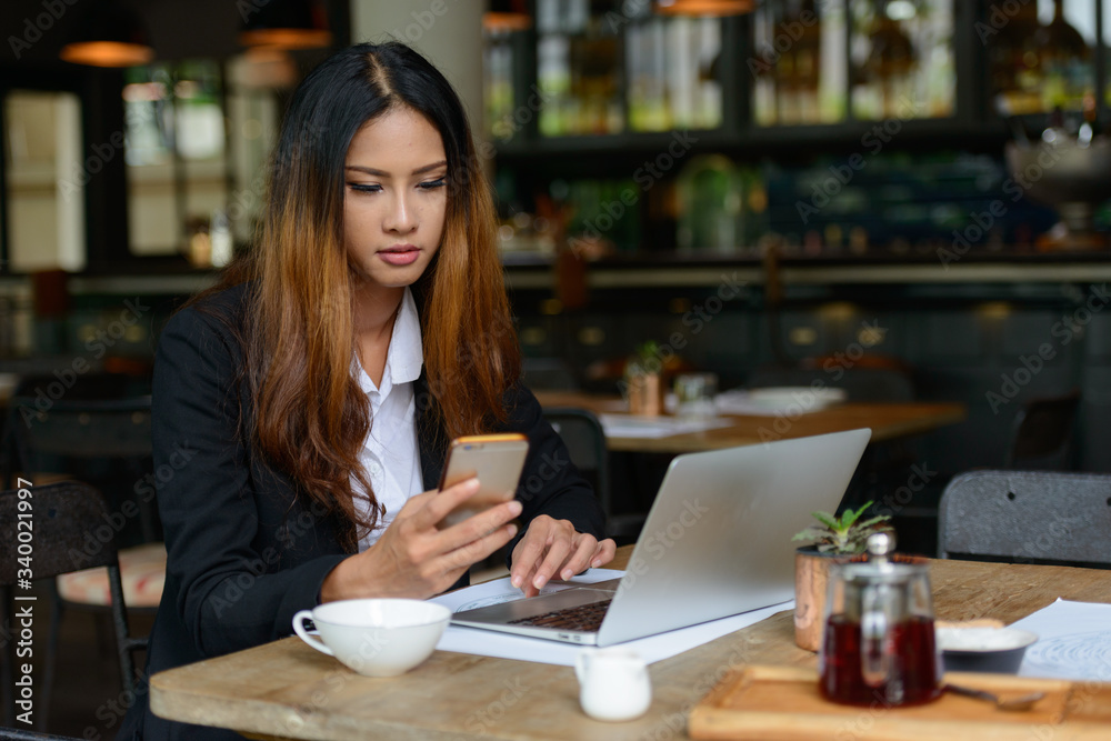 Young beautiful Asian businesswoman using phone at the coffee shop Young beautiful Asian businesswoman using phone at the coffee shop