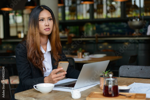 Young beautiful Asian businesswoman using phone at the coffee shop