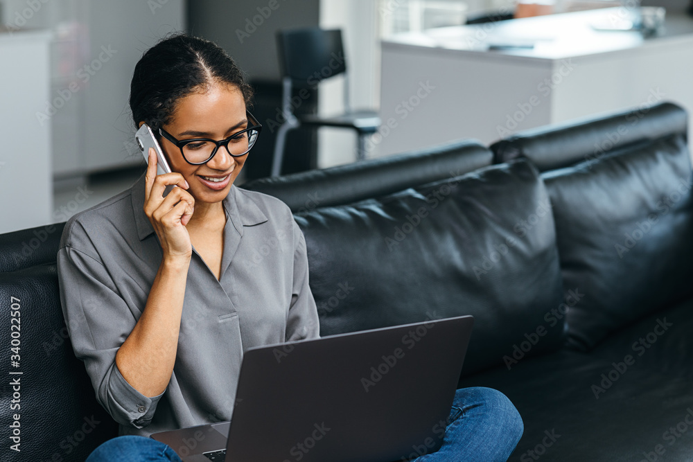 Beautiful woman using a smartphone having phone call from her apartment. Businesswoman enjoying conversation sitting on a couch.