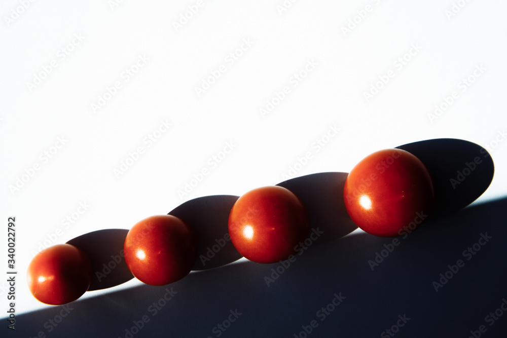 Geometric cherry tomatoes. Four ripe red tomatoes lie in an even row. A smooth black shadow falls from the tomatoes. Tomatoes are placed along the black line in ascending order Geometric cherry tomatoes. Four ripe red tomatoes lie in an even row. A smooth black shadow falls from the tomatoes. Tomatoes are placed along the black line in ascending order