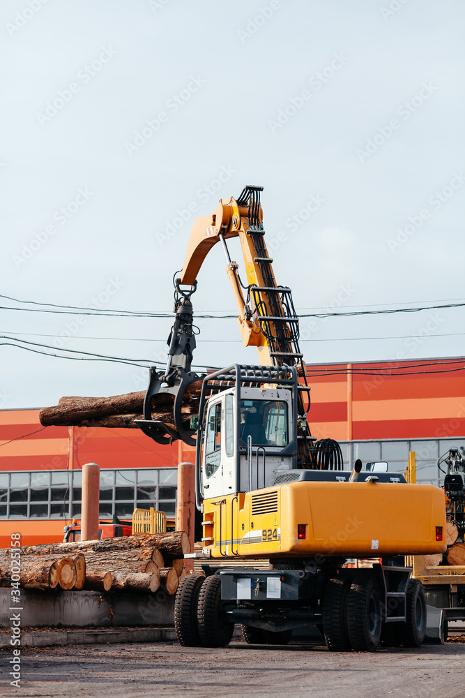 yellow machine excavator shifts logs at a woodworking plant on the street