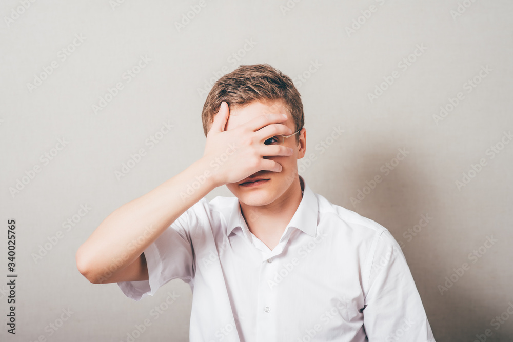 Shocked and terrified. Portrait of young man covering his face by hand and looking at camera while standing against grey background Shocked and terrified. Portrait of young man covering his face by hand and looking at camera while standing against grey background