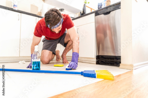 Man kneeling down scrubbing kitchen floor. 