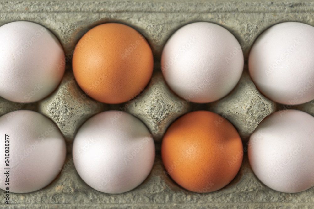 Two orange eggs among white ones in one cardboard package. Top view. Two orange eggs among white ones in one cardboard package. Top view.