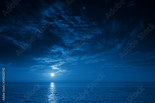 Fototapeta This photo illustration of a deep blue moonlit ocean and sky at night  would make a great travel background for any travel or vacation purpose