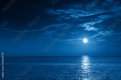 This photo illustration of a deep blue moonlit ocean and sky at night  would make a great travel background for any travel or vacation purpose. © ricardoreitmeyer