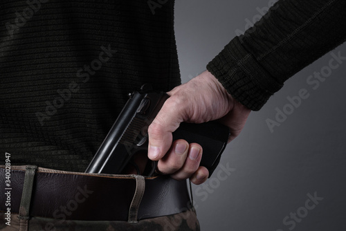 military man holds a gun behind his back in his hand